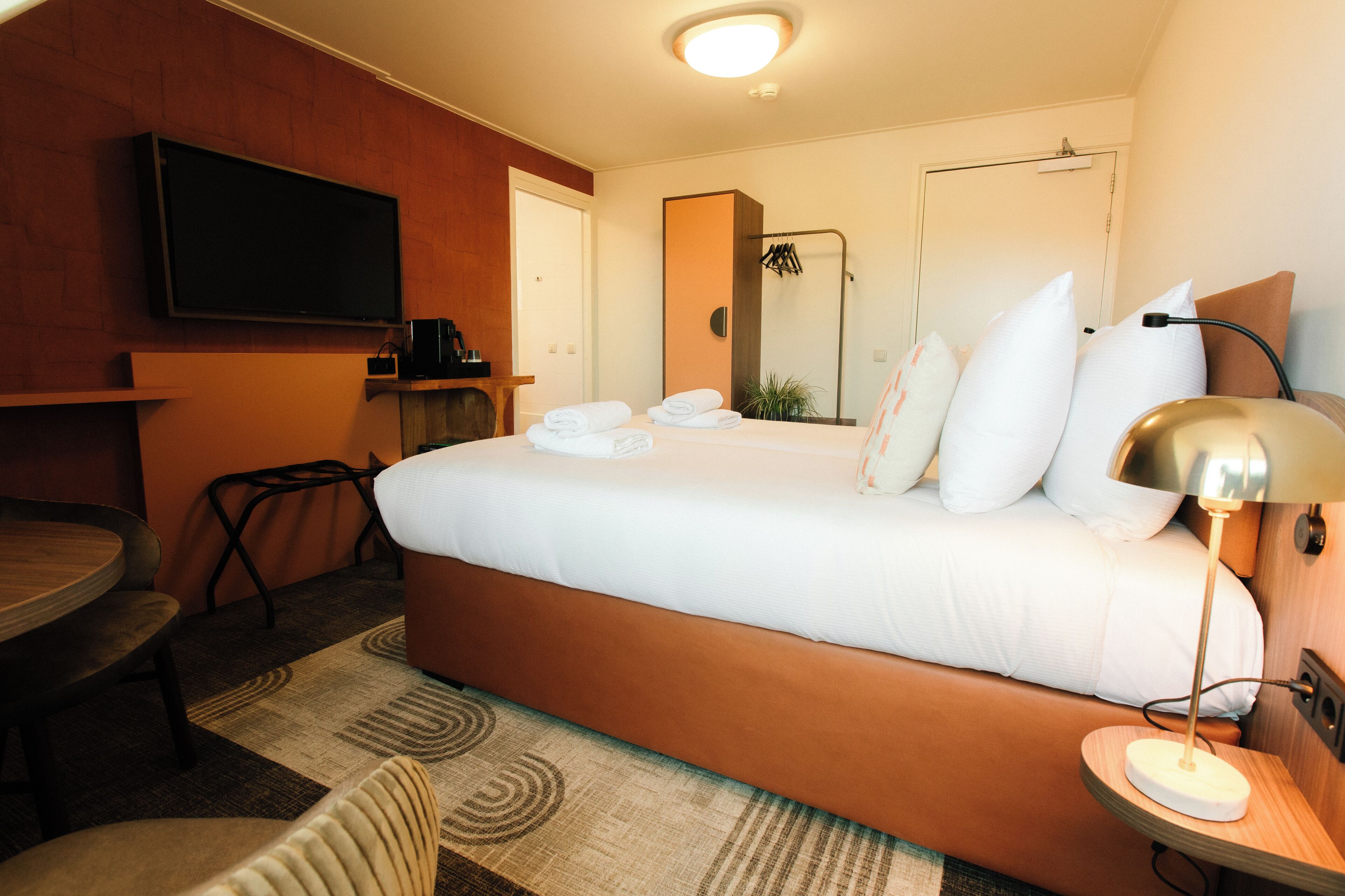 A hotel room with a bed, a TV, a desk, a chair, a lamp, and a mirror.