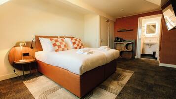 Habitación de hotel con cama, mesita de noche, lámpara y baño visible a través de una puerta abierta.