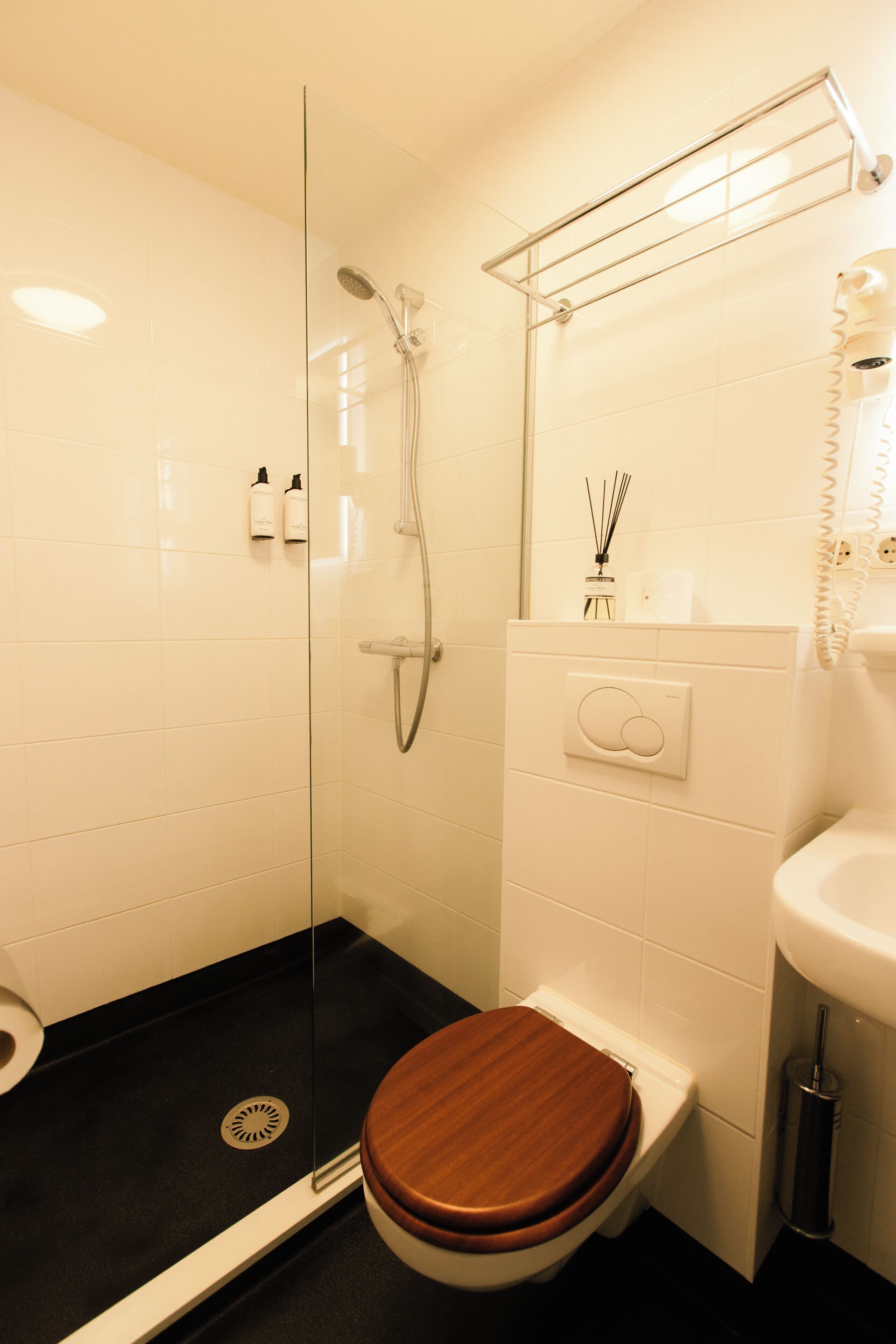 Een badkamer met een douche met glazen wanden, een witte wastafel en een houten toilet.