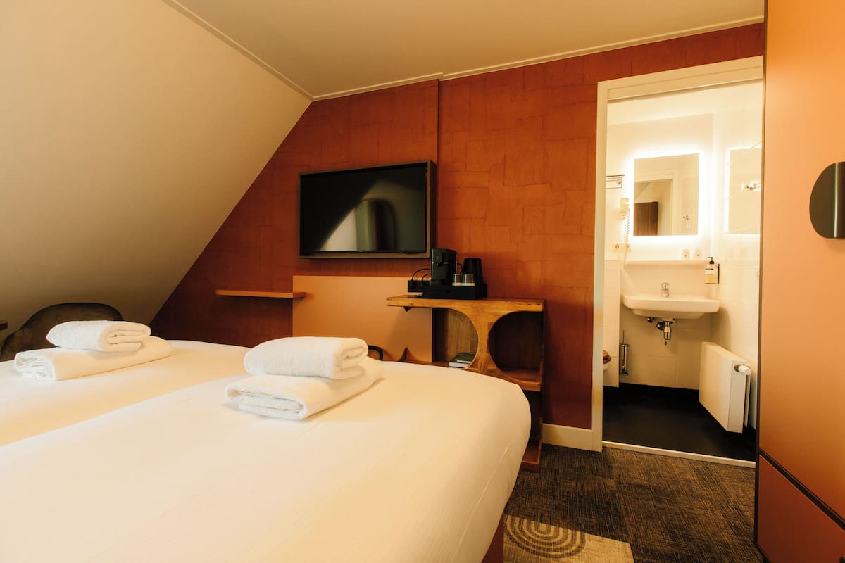 Une chambre d’hôtel comprenant un lit, une télévision, une petite table avec une machine à café, et une salle de bain avec un lavabo et un miroir.