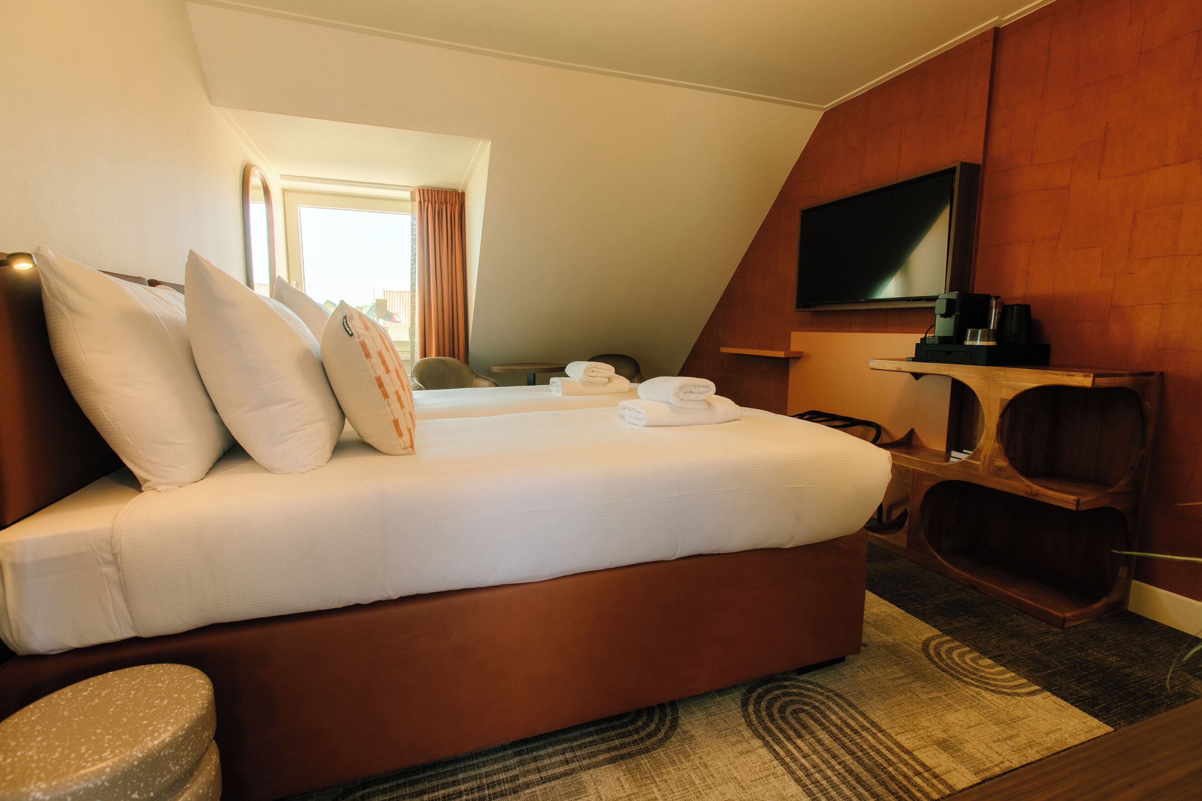 Een hotelkamer met een bed, kussens, een televisie, een koffiezetapparaat en uitzicht op het omliggende landschap.