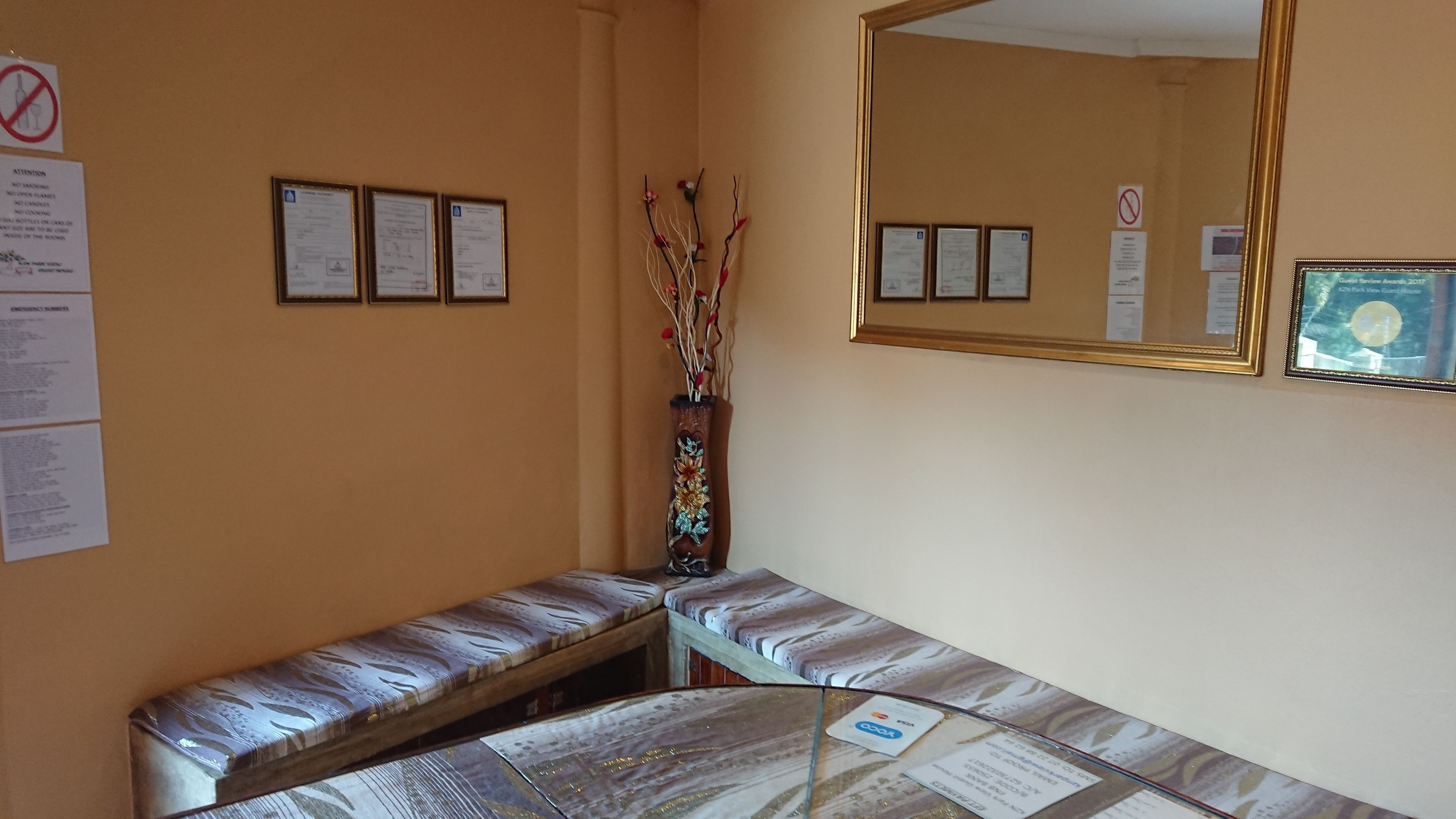 Een hoek van een kamer met een bankje, een spiegel en ingelijste diploma’s aan de muur.