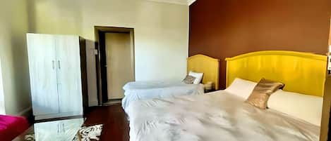 A hotel room with a large bed, a wardrobe, and a door leading to another room.