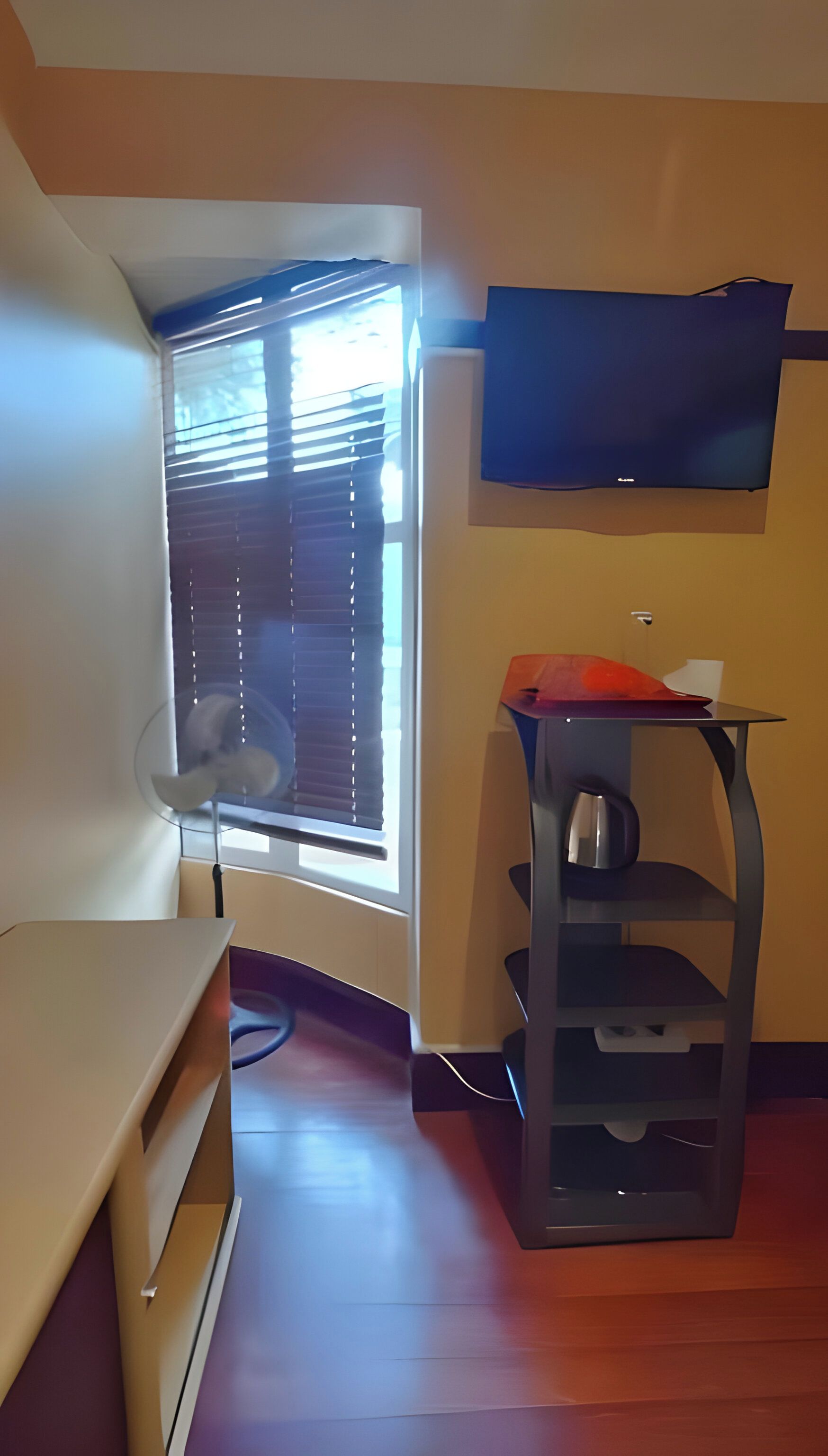 A room with a window, a flat-screen TV mounted on the wall, a desk, and a chair.