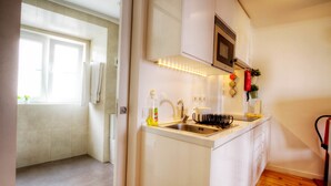 Een moderne keuken met witte kastjes, een roestvrijstalen spoelbak en een magnetron. Er is een raam dat voor natuurlijk licht zorgt, en een houten vloer is zichtbaar.