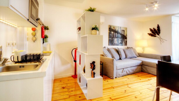 Een moderne woonkamer met een keukenhoek, een grijze bank, een eettafel en een houten vloer.