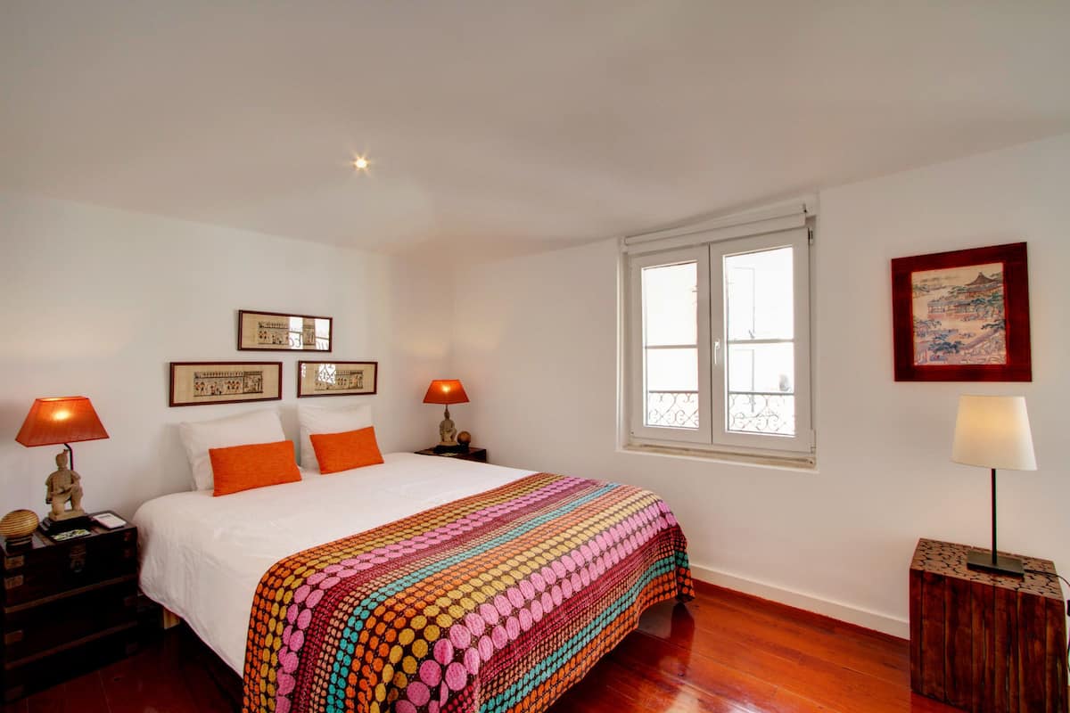 Une chambre à coucher bien aménagée, avec un grand lit, deux tables de chevet avec des lampes, une fenêtre donnant sur un beau paysage et des tableaux encadrés accrochés aux murs.