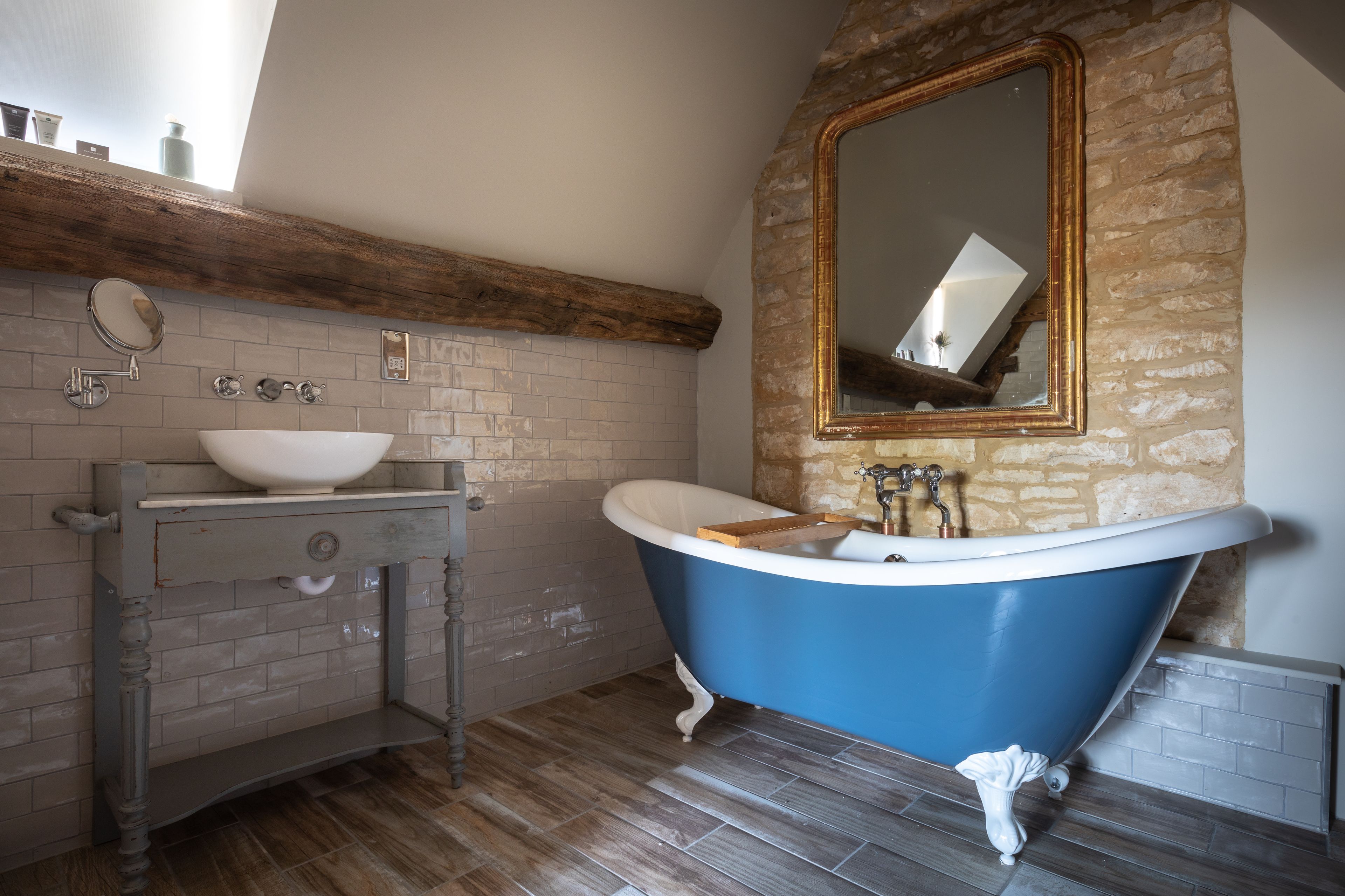 A bathroom with a freestanding bathtub, a sink with a mirror, and a wooden shelf above the sink.