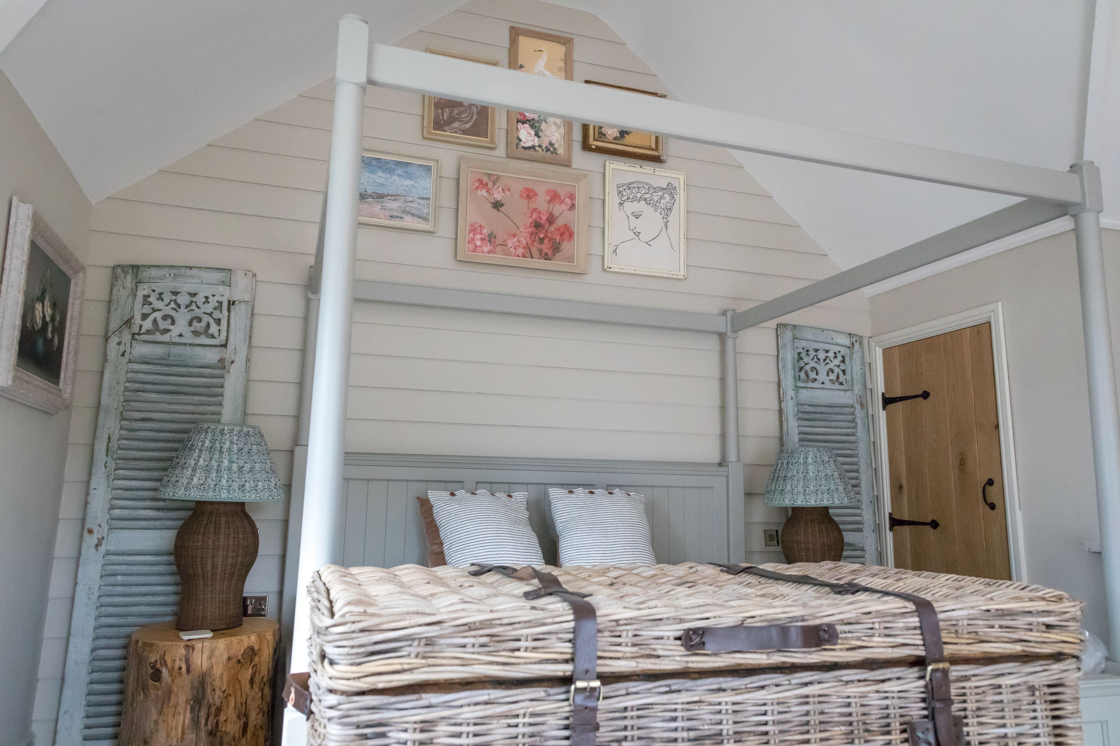 Un dormitorio con una cama, dos almohadas, una mesita de noche, una lámpara y una pared con cuadros.