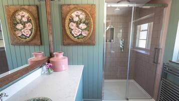 Une salle de bain avec une douche à parois de verre, un meuble-lavabo avec un miroir et deux tableaux à motifs floraux encadrés.