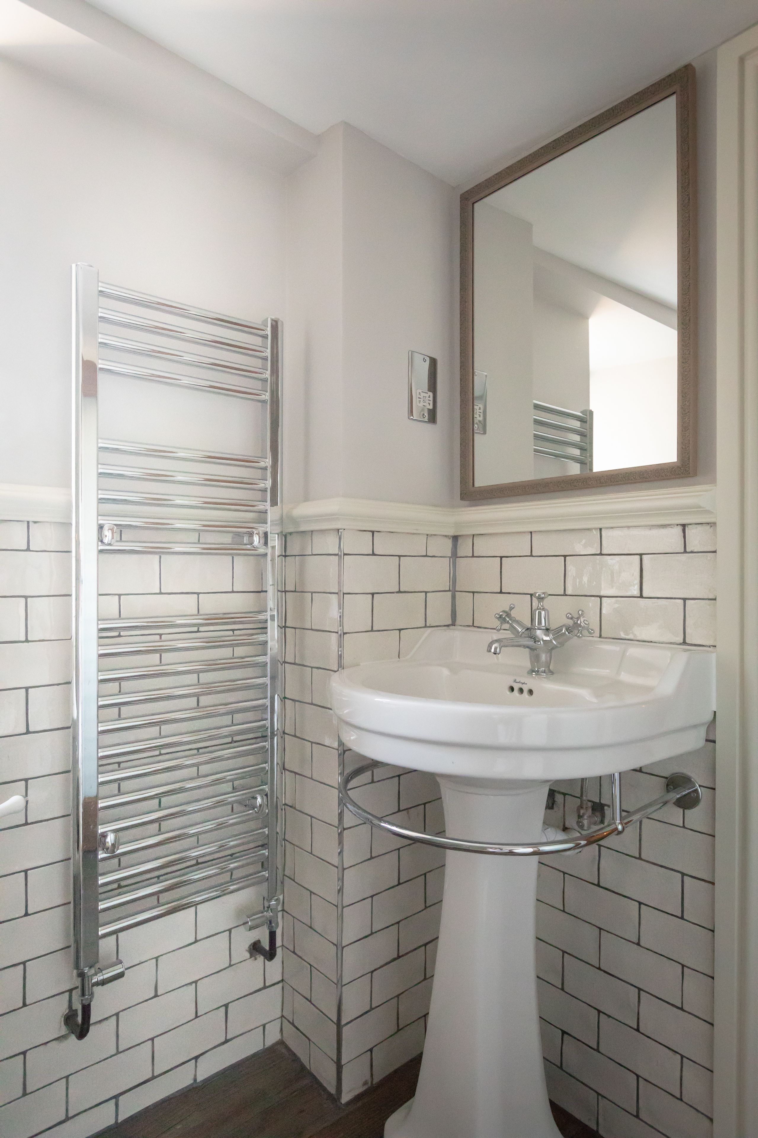 A bathroom with a white pedestal sink, a chrome towel rack, and a large mirror above the sink.