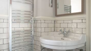 A bathroom with a white pedestal sink, a chrome towel rack, and a large mirror above the sink.