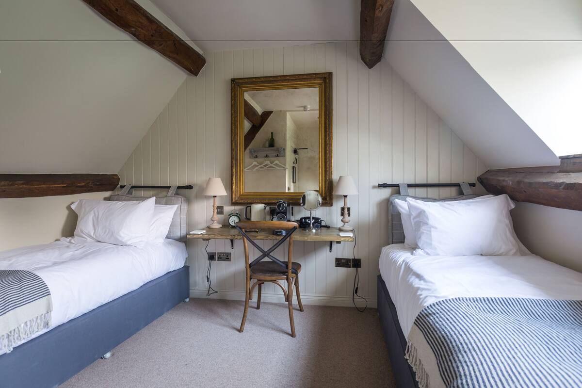 A bedroom with two beds, a desk, a chair, and a mirror.