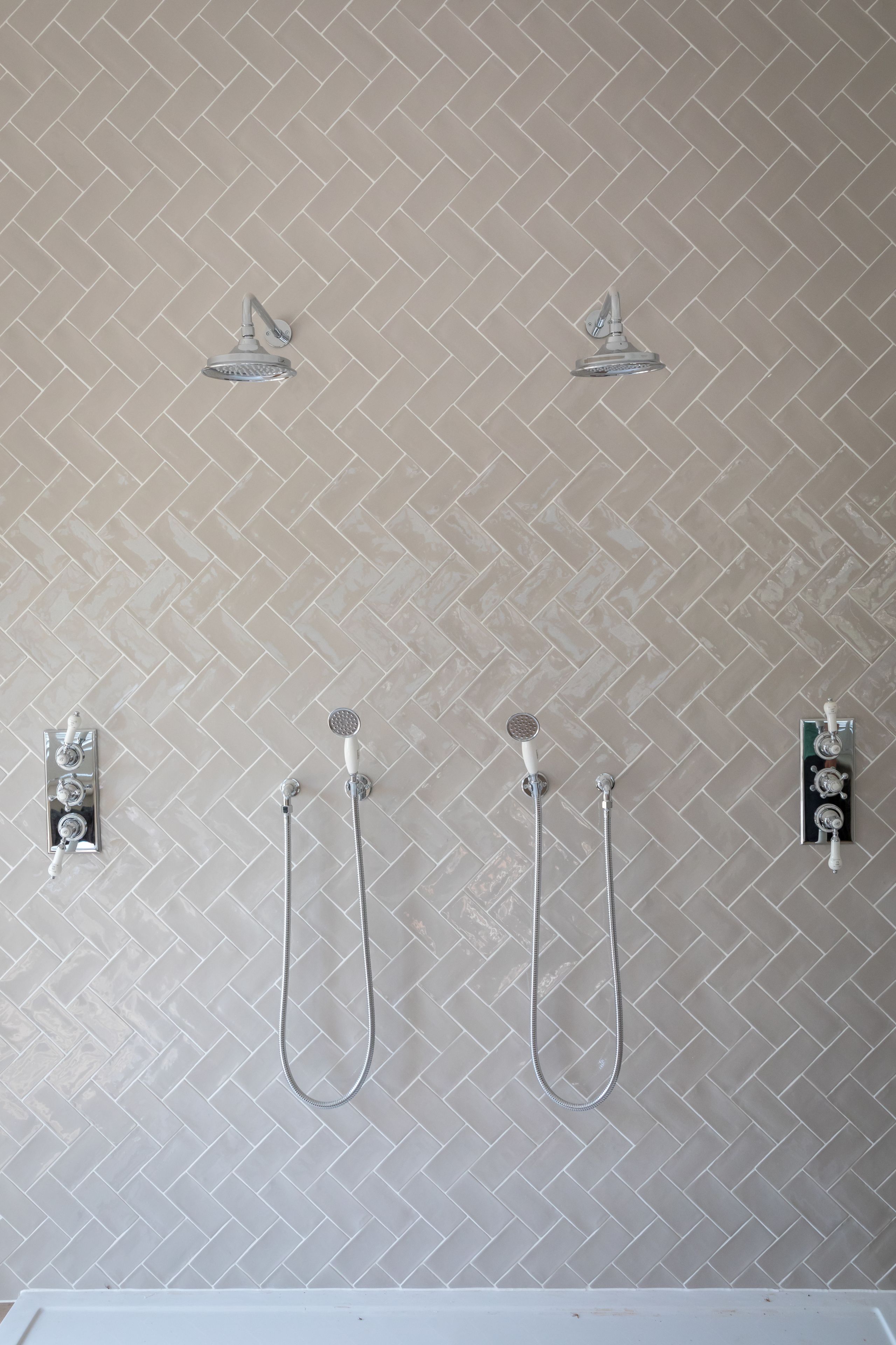 A bathroom with a herringbone tile pattern, a showerhead, and two handheld showerheads mounted on the wall.
