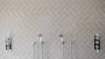 A bathroom with a herringbone tile pattern, a showerhead, and two handheld showerheads mounted on the wall.