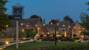 A traditional stone building with a sign reading "Frogmill" and "Brakspear." It features outdoor seating and a well-lit patio area. - The Frogmill (Cheltenham)