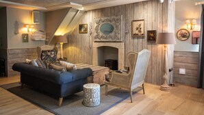 A cozy living room with a sofa, armchair, and ottoman, wooden walls, a fireplace, and wall-mounted lamps. - The Frogmill (Cheltenham)