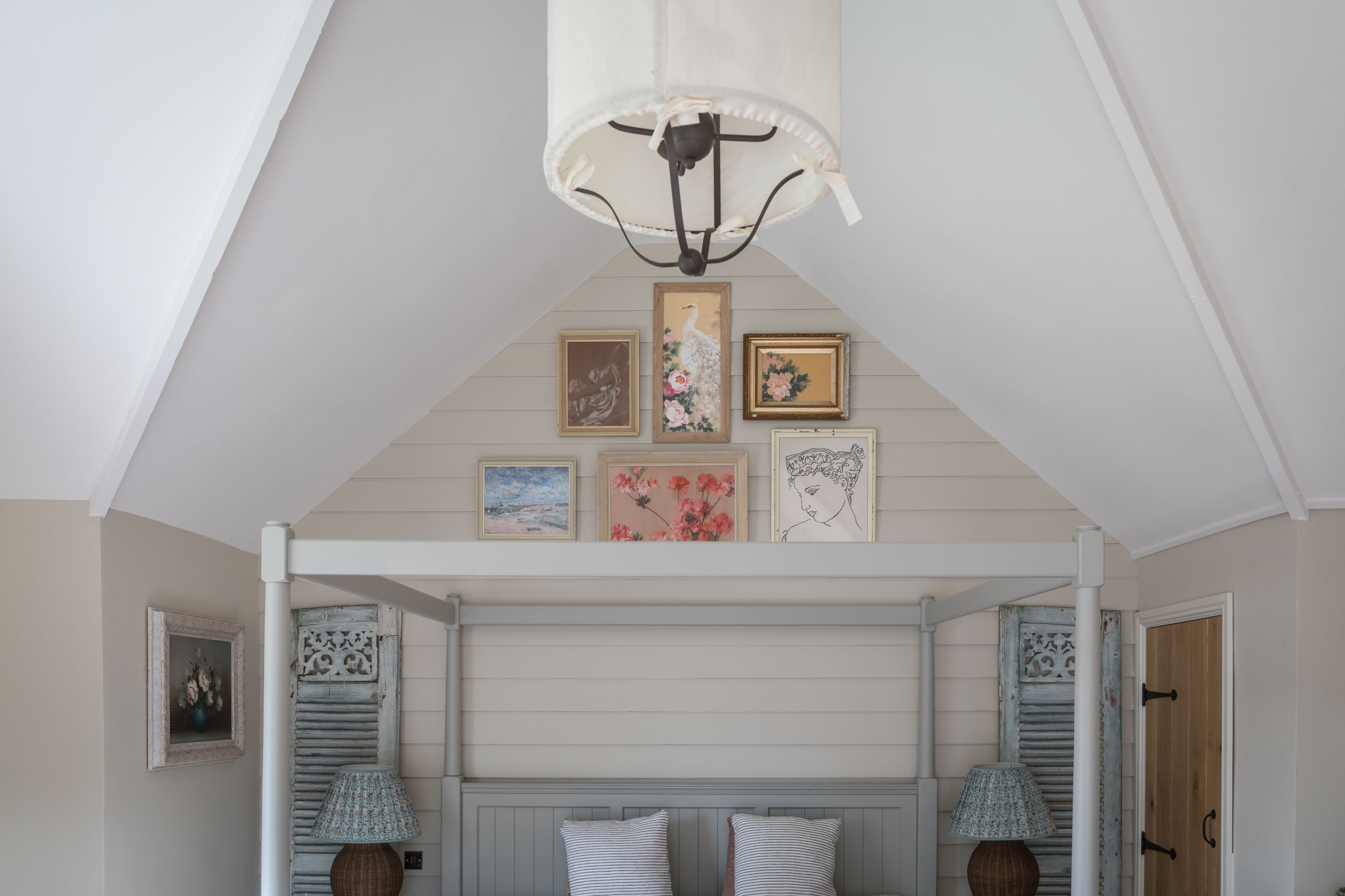 A bedroom with a sloped ceiling, a bed with a headboard, and wall-mounted artwork.