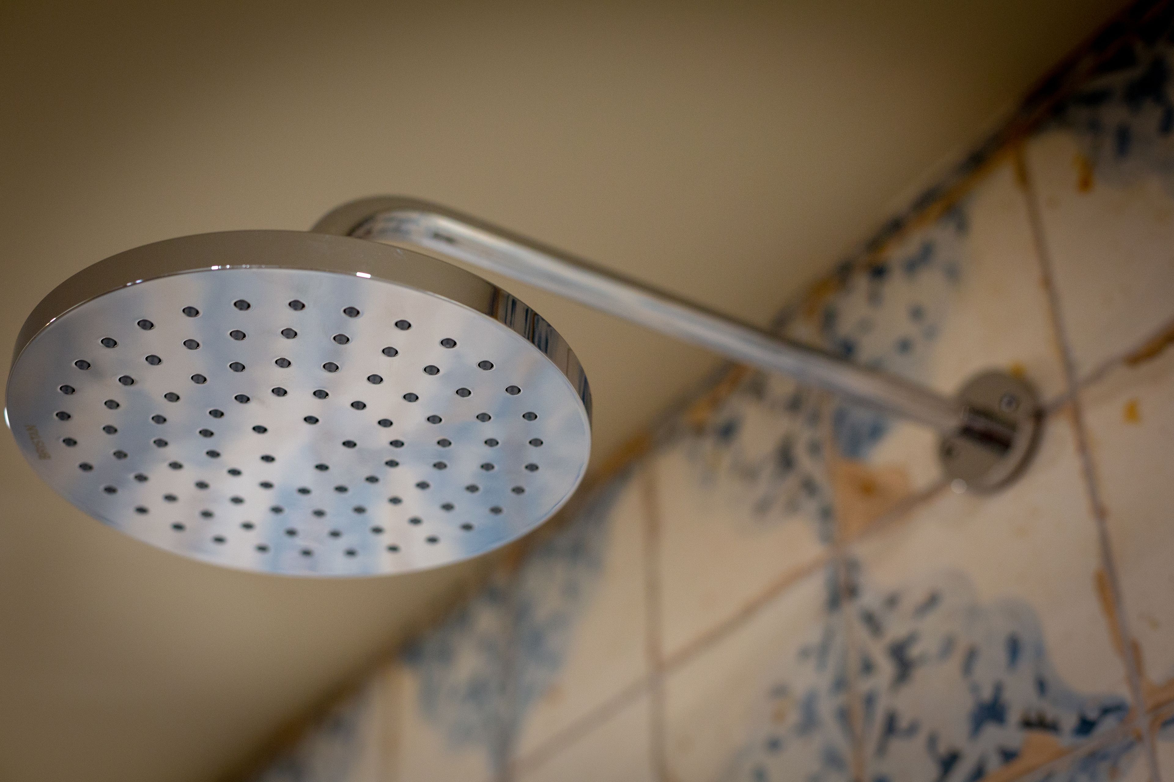 A showerhead with a perforated design, mounted on a wall with a patterned tile backsplash.