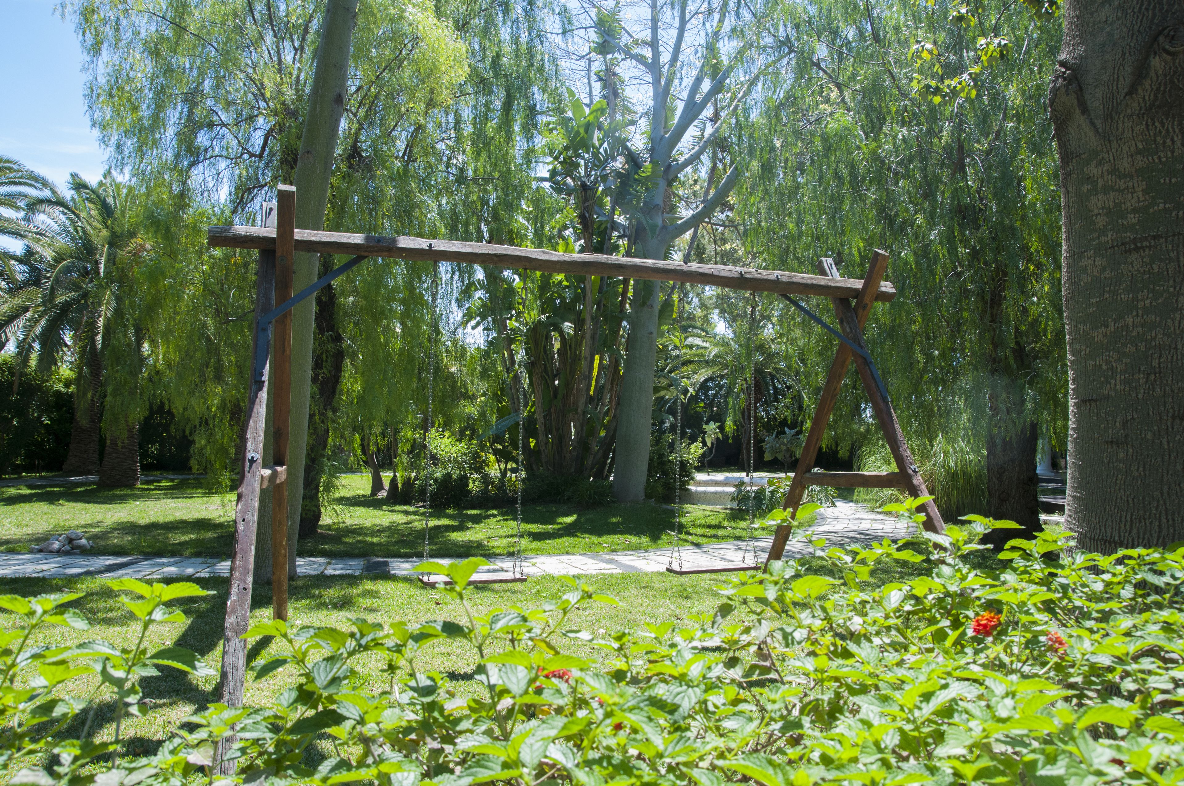 A wooden swing set in a lush garden with trees and greenery.