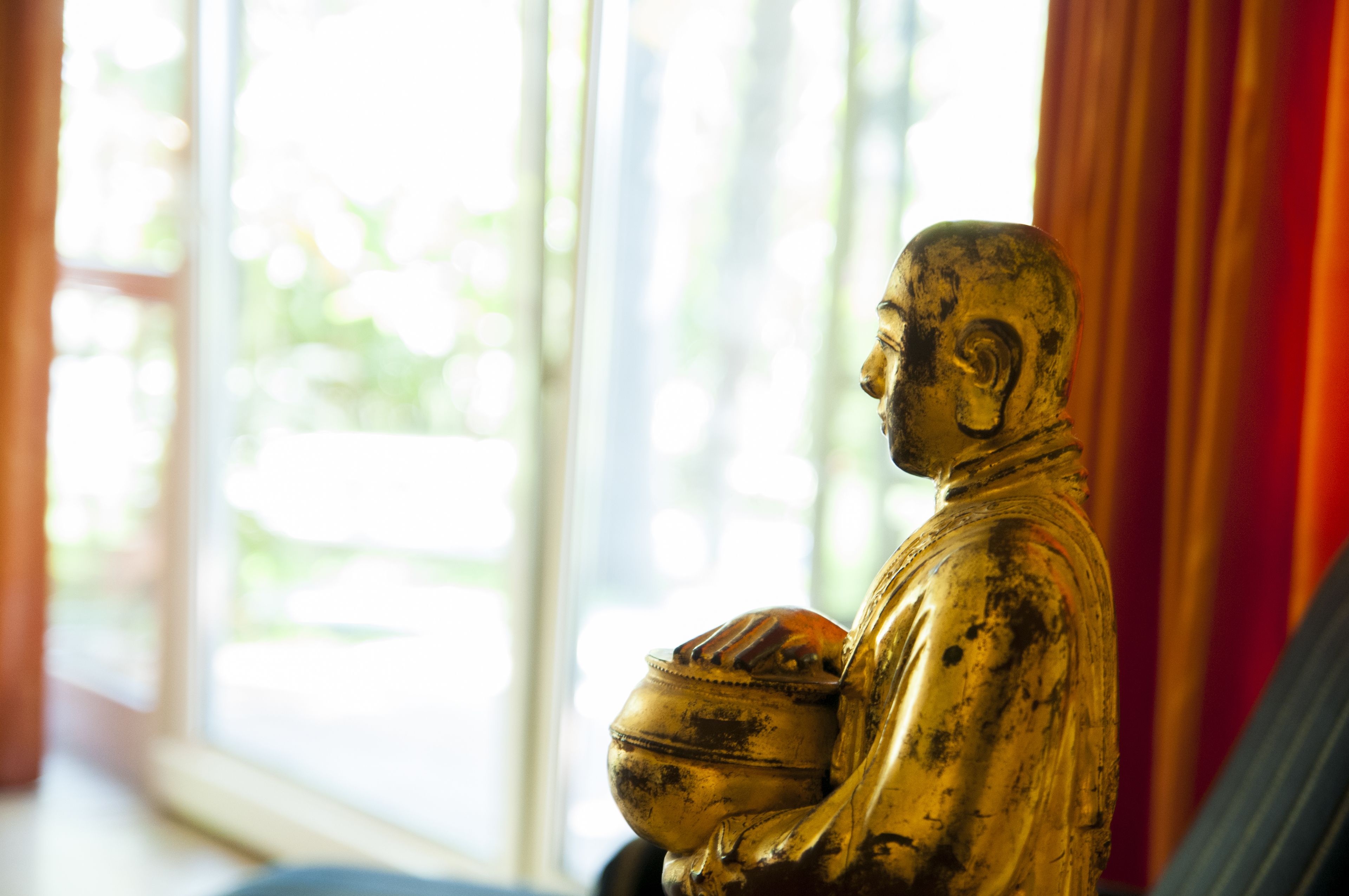 A statue in a room with a large window and curtains.