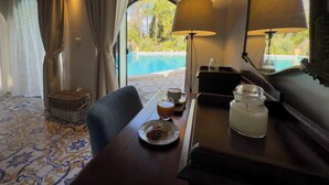 A room with a view of a swimming pool, a dining table with a plate of food and a glass of drink, a lamp, and a mirror. - La Villa (Giardini Naxos)