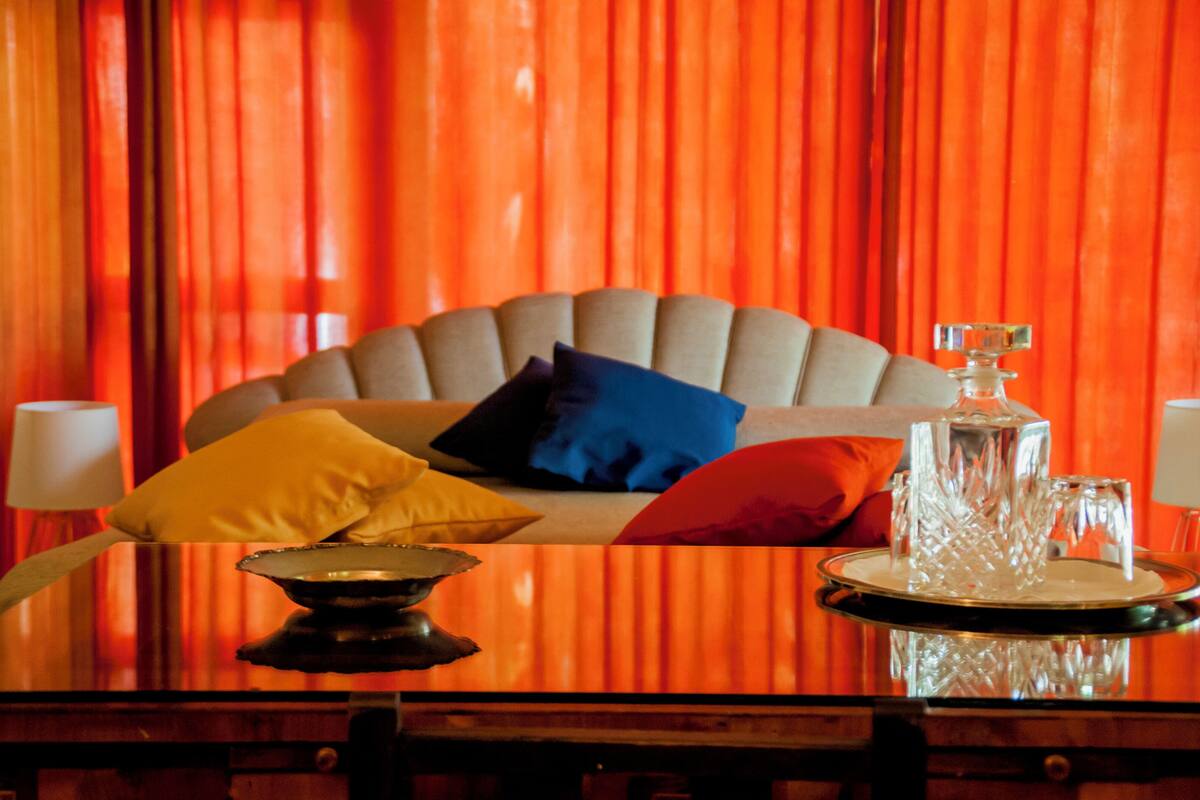 Una cama con cabecera, almohadas, una bandeja con un decantador de vidrio y una lámpara de mesa.