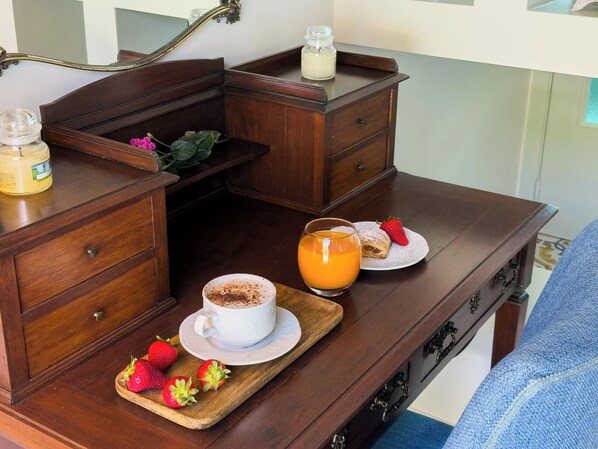A wooden desk with a cup of coffee, a glass of orange juice, a plate with a pastry and strawberries, and a jar of jam.
