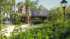 A courtyard with a stone building, palm trees, and a pathway leading to the entrance. - La Villa (Giardini Naxos)