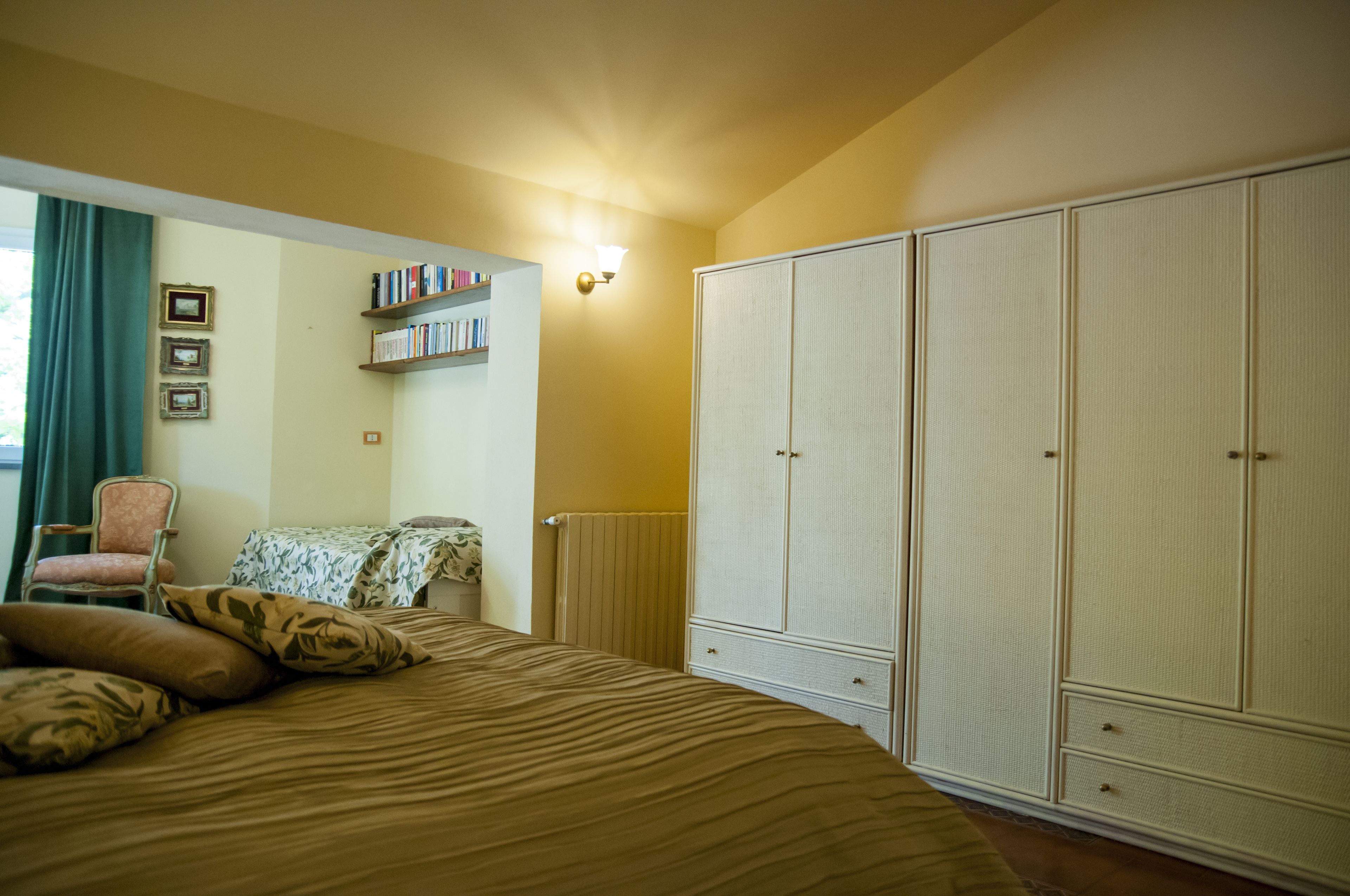 A bedroom with a bed, a chair, a wardrobe, and a bookshelf.