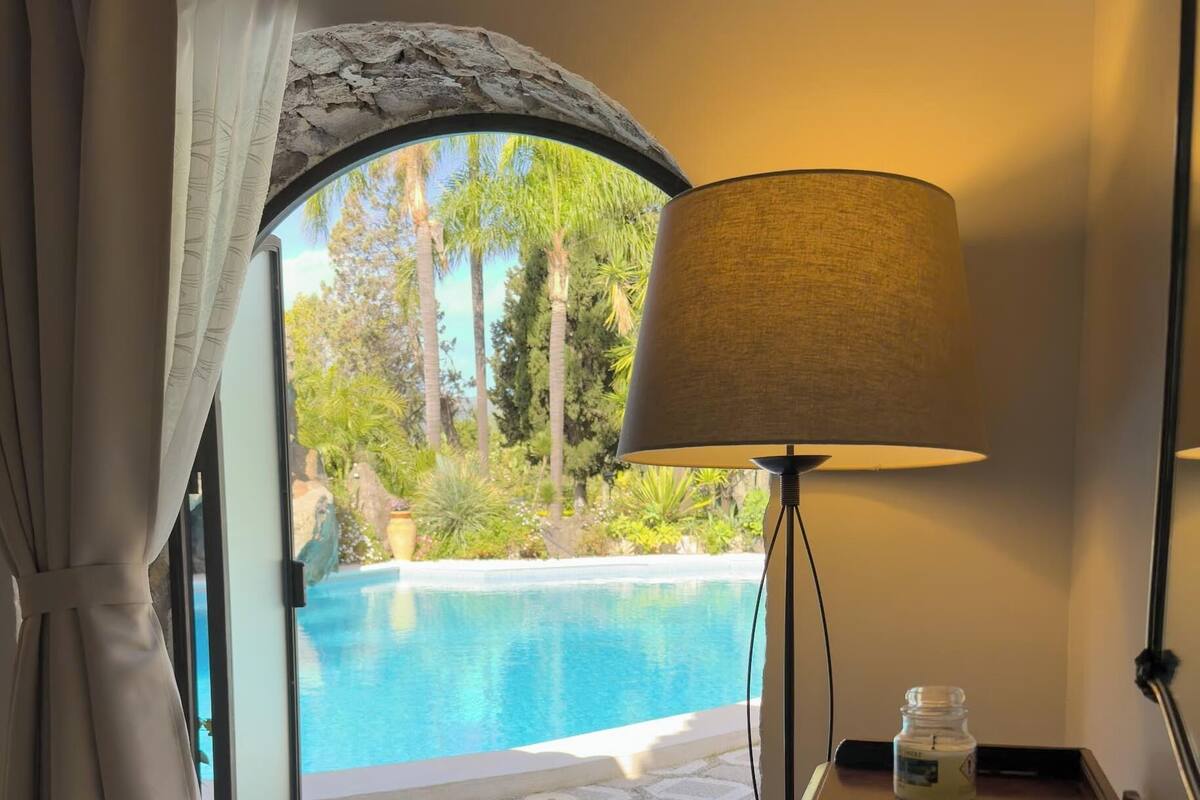 Una habitación con vista a una piscina, una mesa con una lámpara, un vaso de jugo de naranja, un plato de comida y una botella de leche.