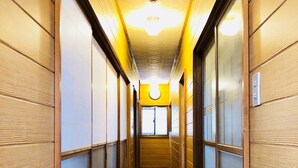 A narrow, well-lit hallway with wooden paneling and a polished floor, leading to a bright room with a large window. - Asahi (Fujiyoshida)