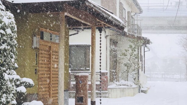 A residential street with houses covered in snow, featuring traditional architecture with wooden elements and a covered porch. - Asahi (Fujiyoshida)