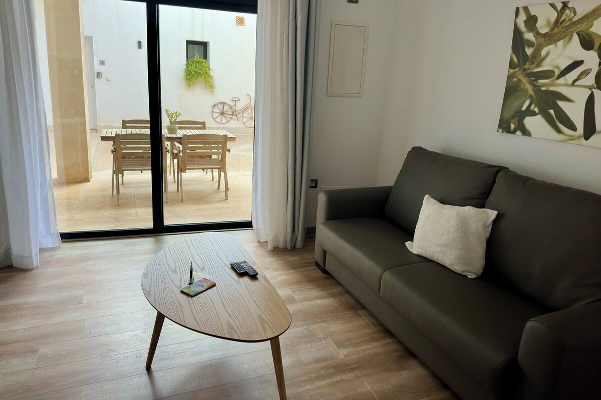 Ett modernt vardagsrum med ett soffbord i trä, en mörkgrön soffa och en skjutdörr i glas som leder ut till en uteplats med ett bord och stolar.