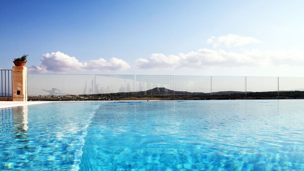 Una piscina blava i cristal·lina amb vista a un paisatge llunyà i una tanca.