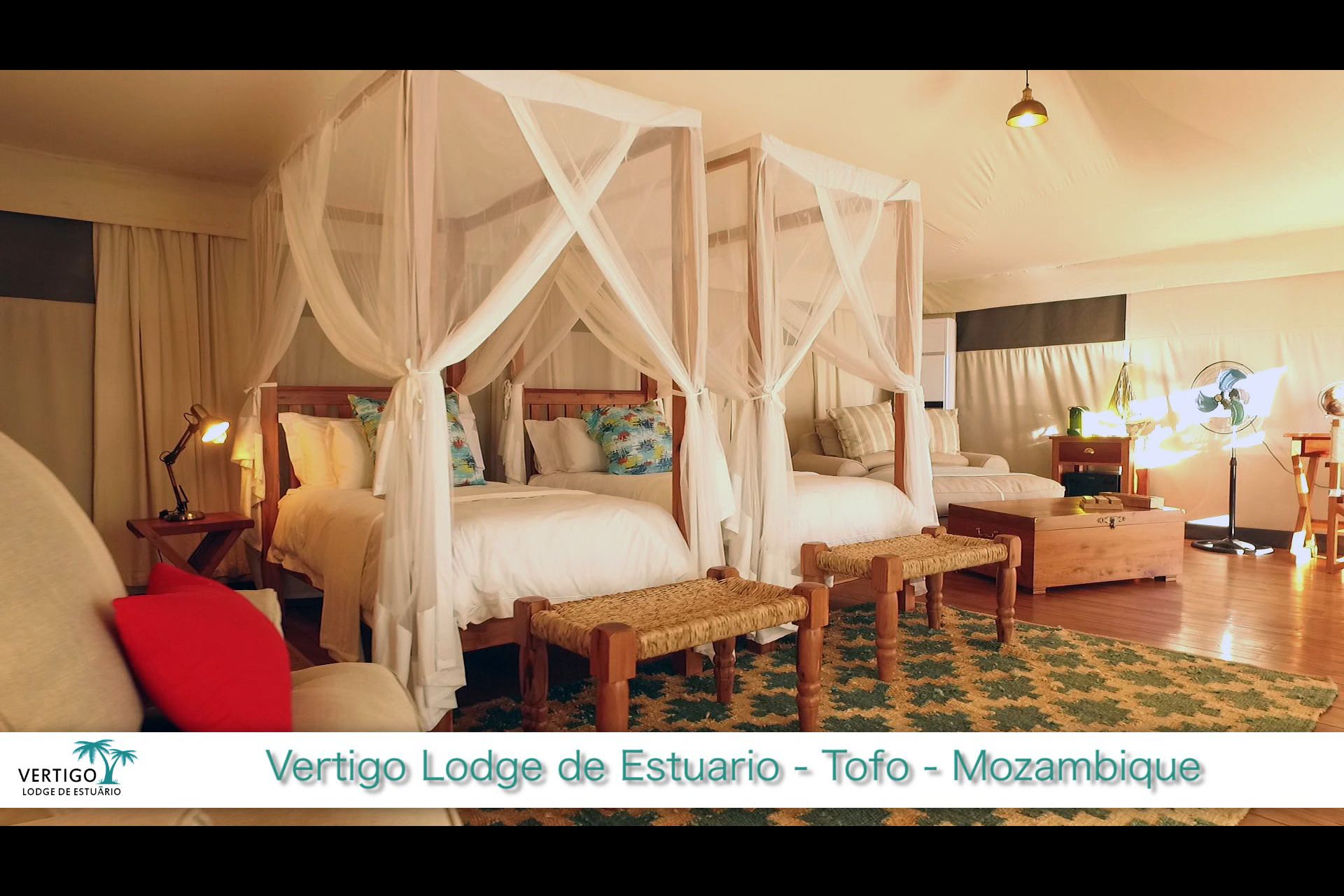 A bedroom with a four-poster canopy bed, two bedside tables, a wooden bench, and a nightstand with a lamp.