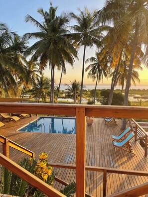Une terrasse en bois avec une piscine, des palmiers et une vue sur l’océan.