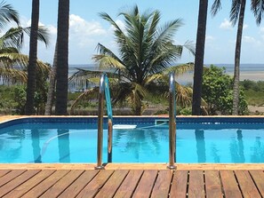 A swimming pool with wooden deck, metal railings, and palm trees in the background. - Vertigo Lodge de Estuario (Inhambane)