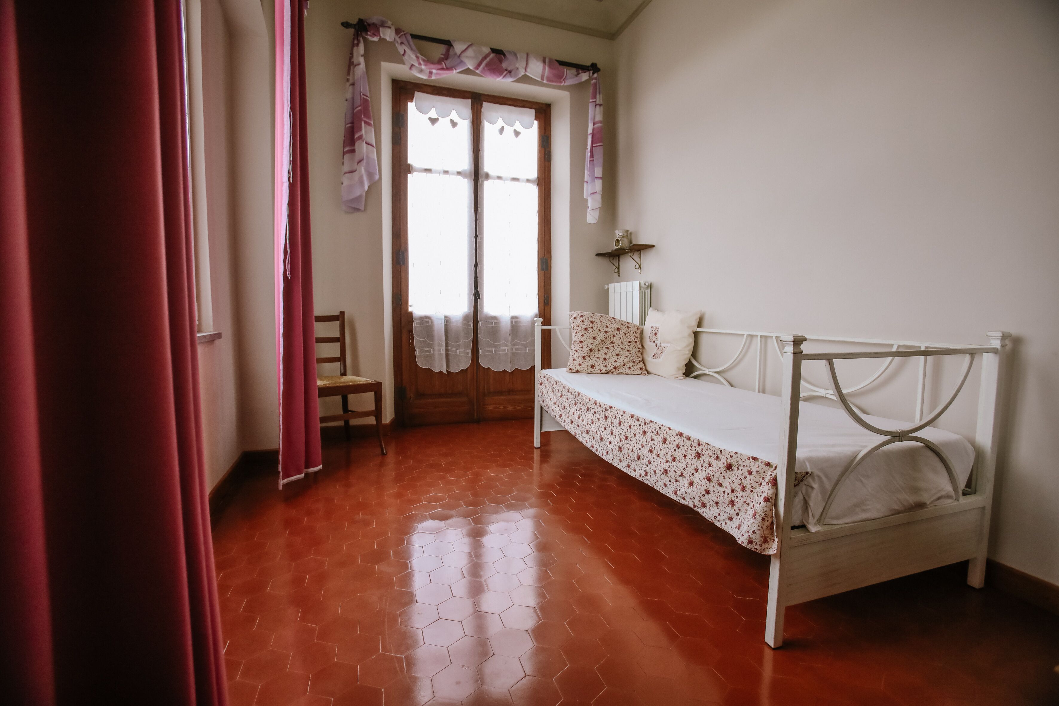 A bedroom with a bed, a chair, a radiator, and a door with curtains.