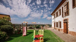 A children's play area with a slide and climbing structure, adjacent to a building with a brick facade and wooden shutters. - Il Pozzo Fiorito Residence (Cossombrato)