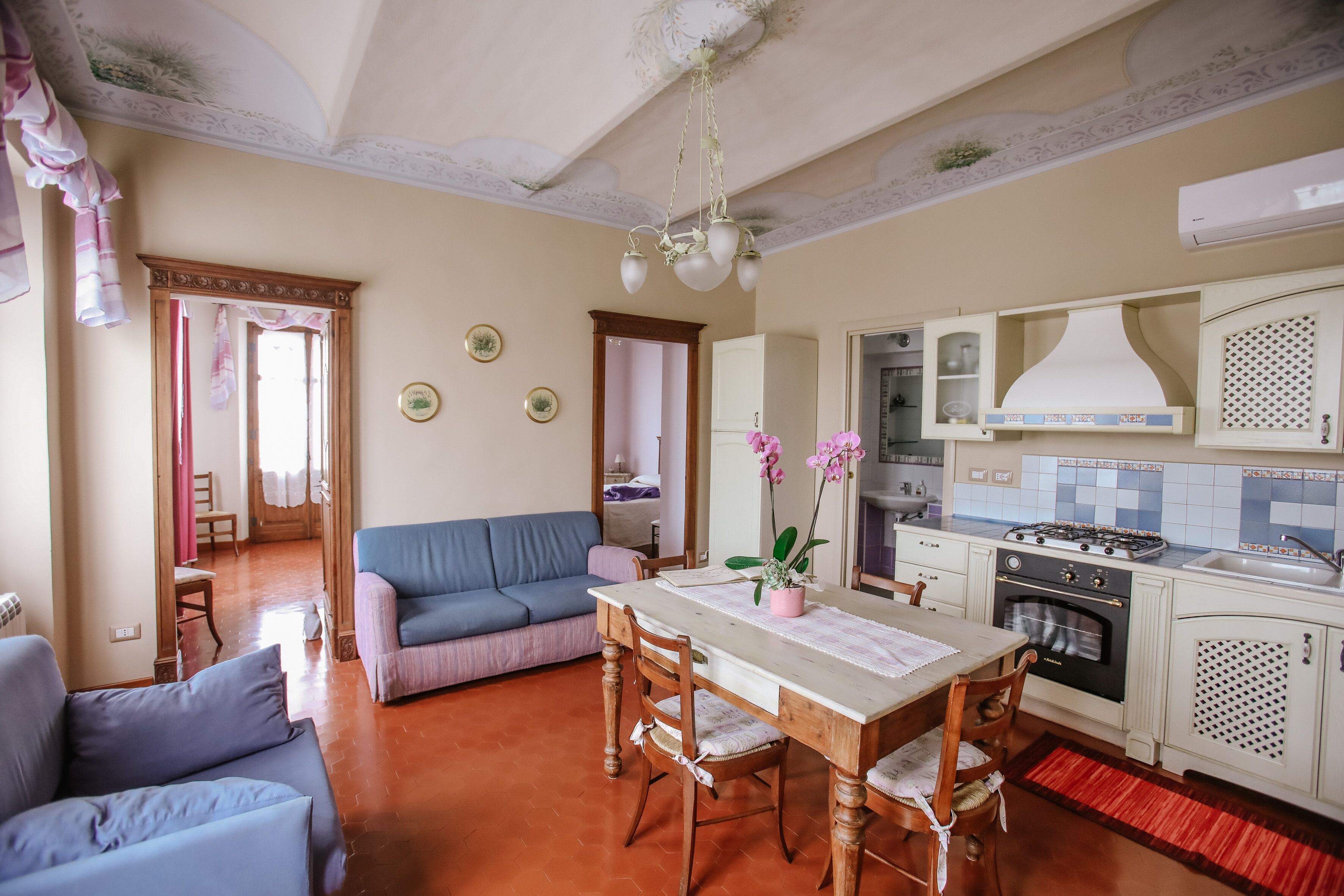A cozy living room with a blue sofa, a wooden dining table with chairs, and a kitchen area with white cabinets and a stove.