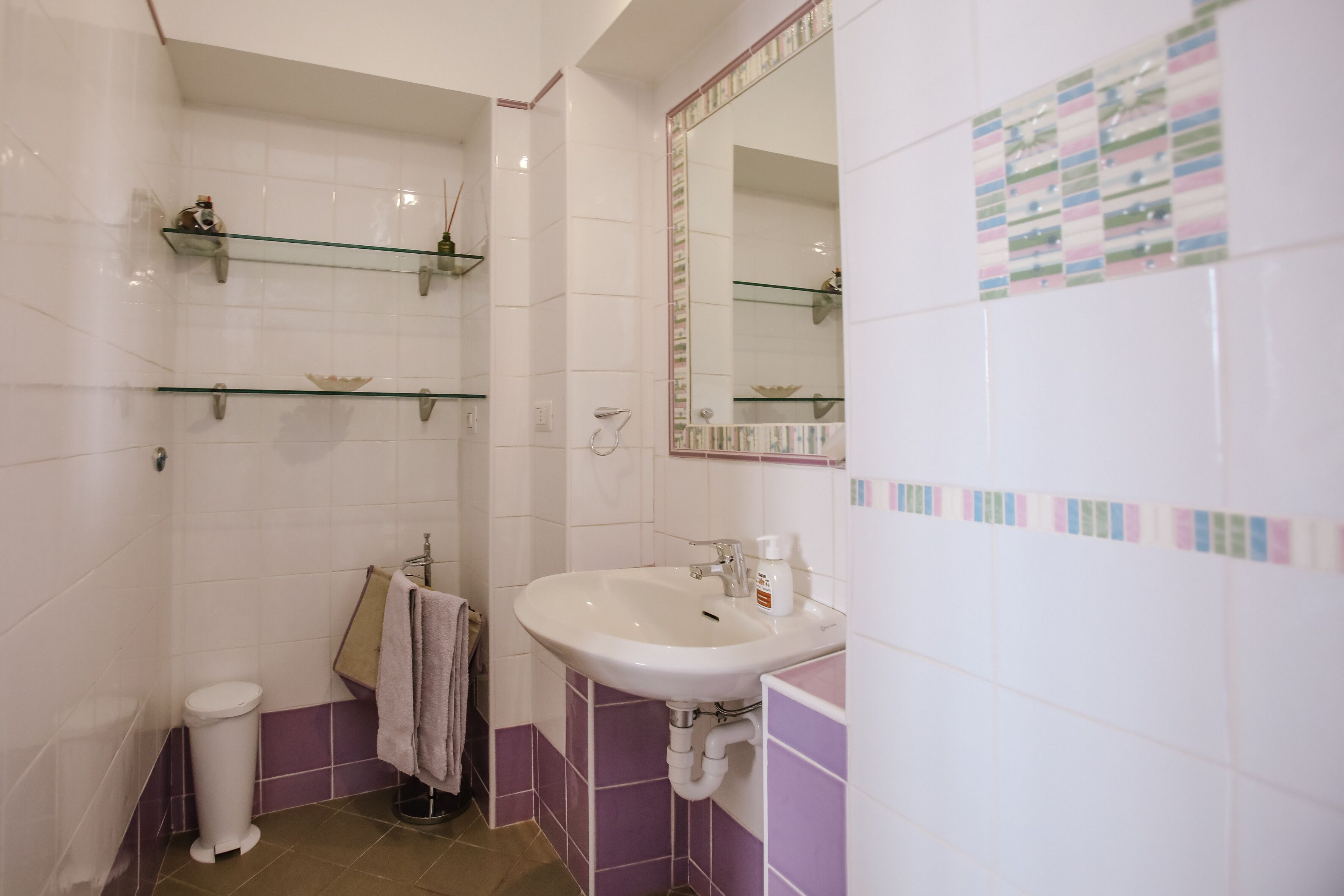 A bathroom with a white sink, a mirror, and shelves with toiletries.