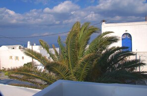 A white building with a blue door, surrounded by palm trees. - Villa Renieris (Santorini)
