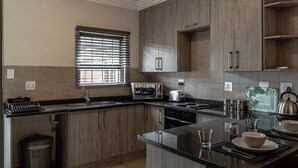 A modern kitchen with wooden cabinets, a built-in oven, and a granite countertop. - Camelot Guest House & Apartments (Potchefstroom)