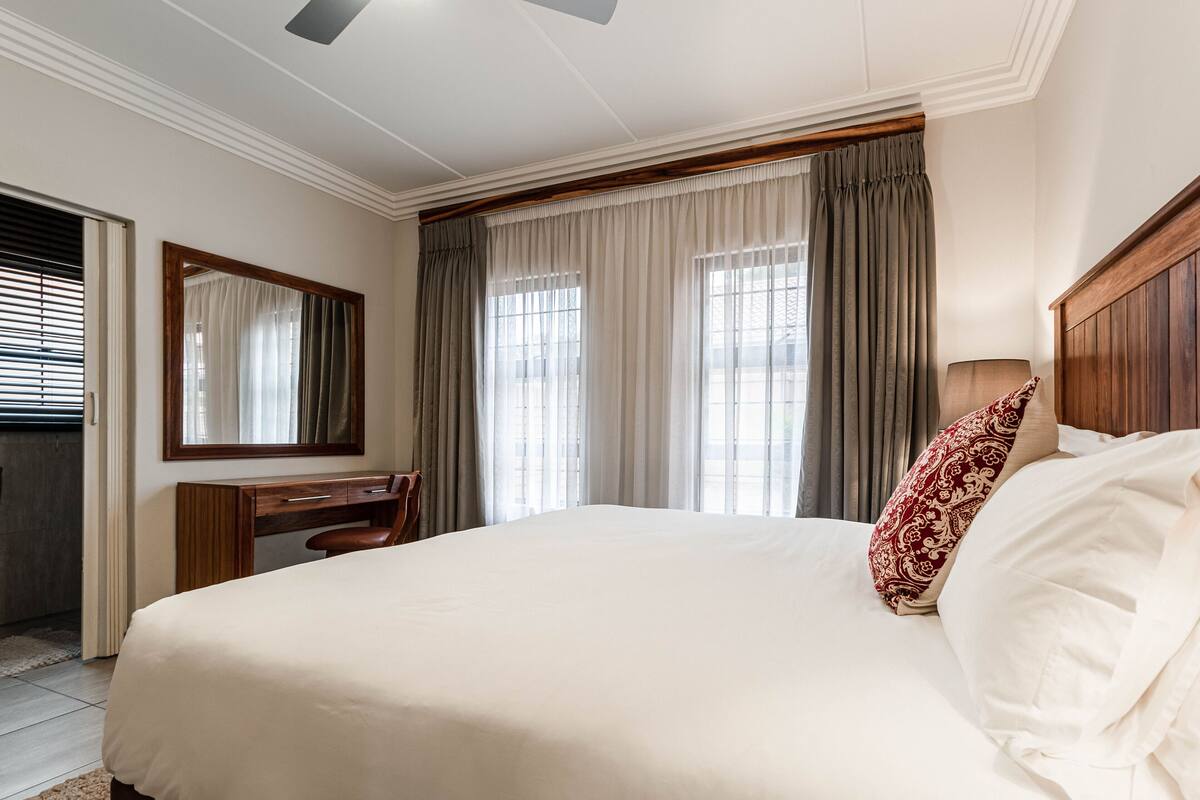 A hotel room with a large bed, a wooden desk, a chair, and a mirror.