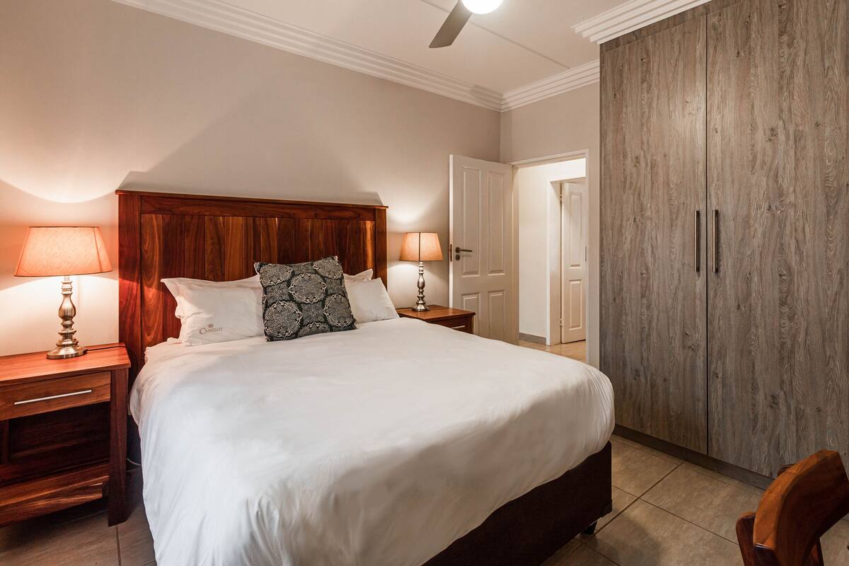 A neatly made bed with white linens, two bedside lamps, and a wooden headboard.