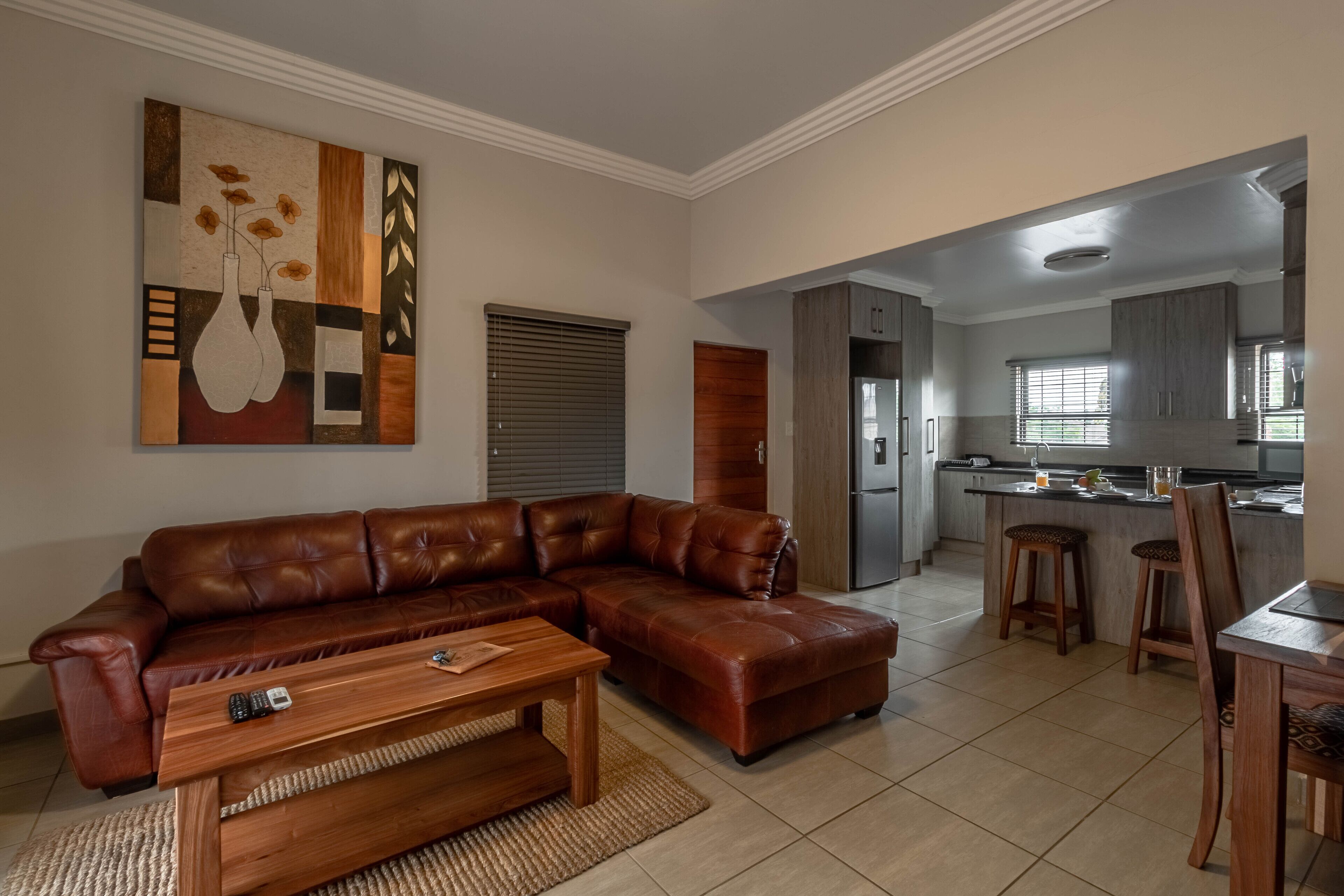 A living room with a brown leather sectional sofa, a wooden coffee table, and a painting on the wall.