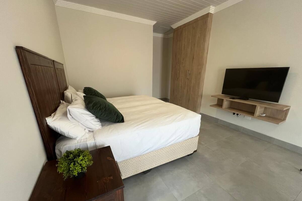 A bedroom with a bed, a TV on a wooden shelf, and a wardrobe.