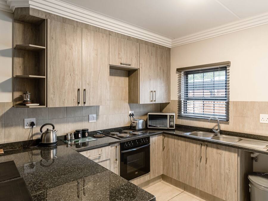 Una cucina moderna con mobili in legno, un piano di lavoro in granito, forno integrato, microonde e una finestra con persiane.