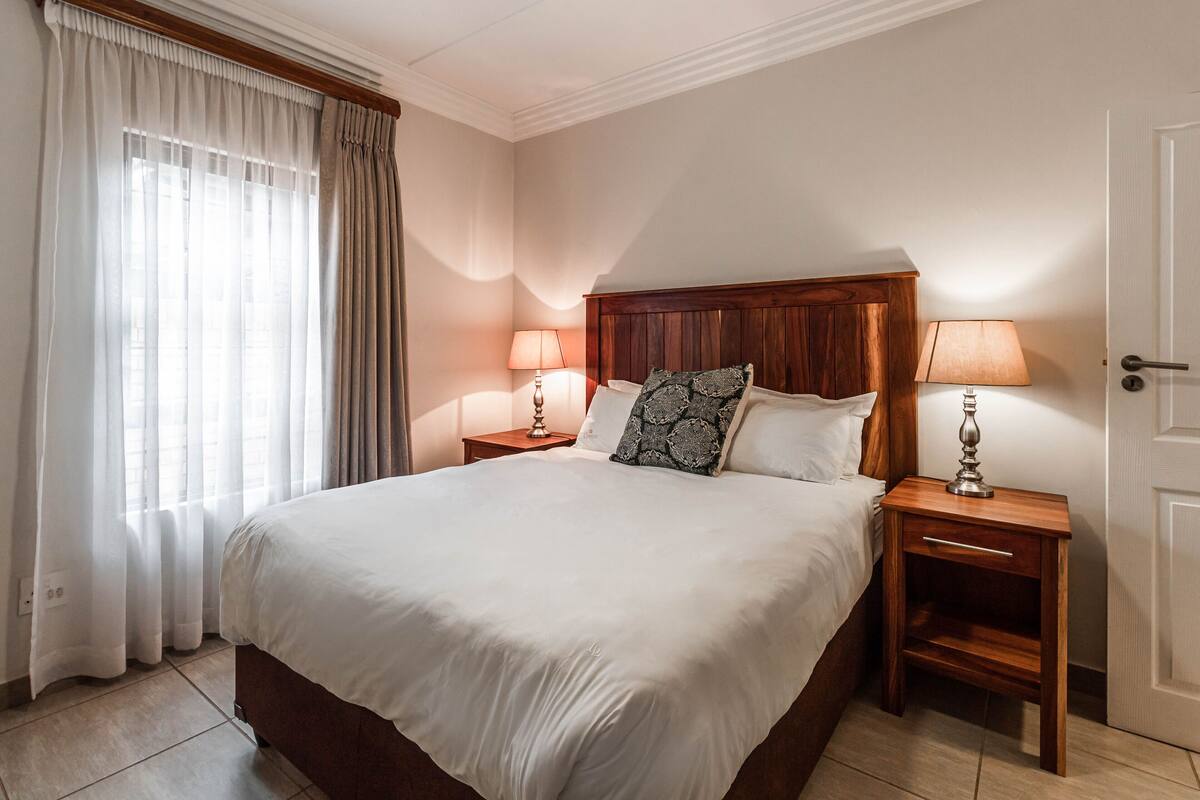 A hotel room with a large bed, two bedside tables with lamps, a wooden headboard, and a door.